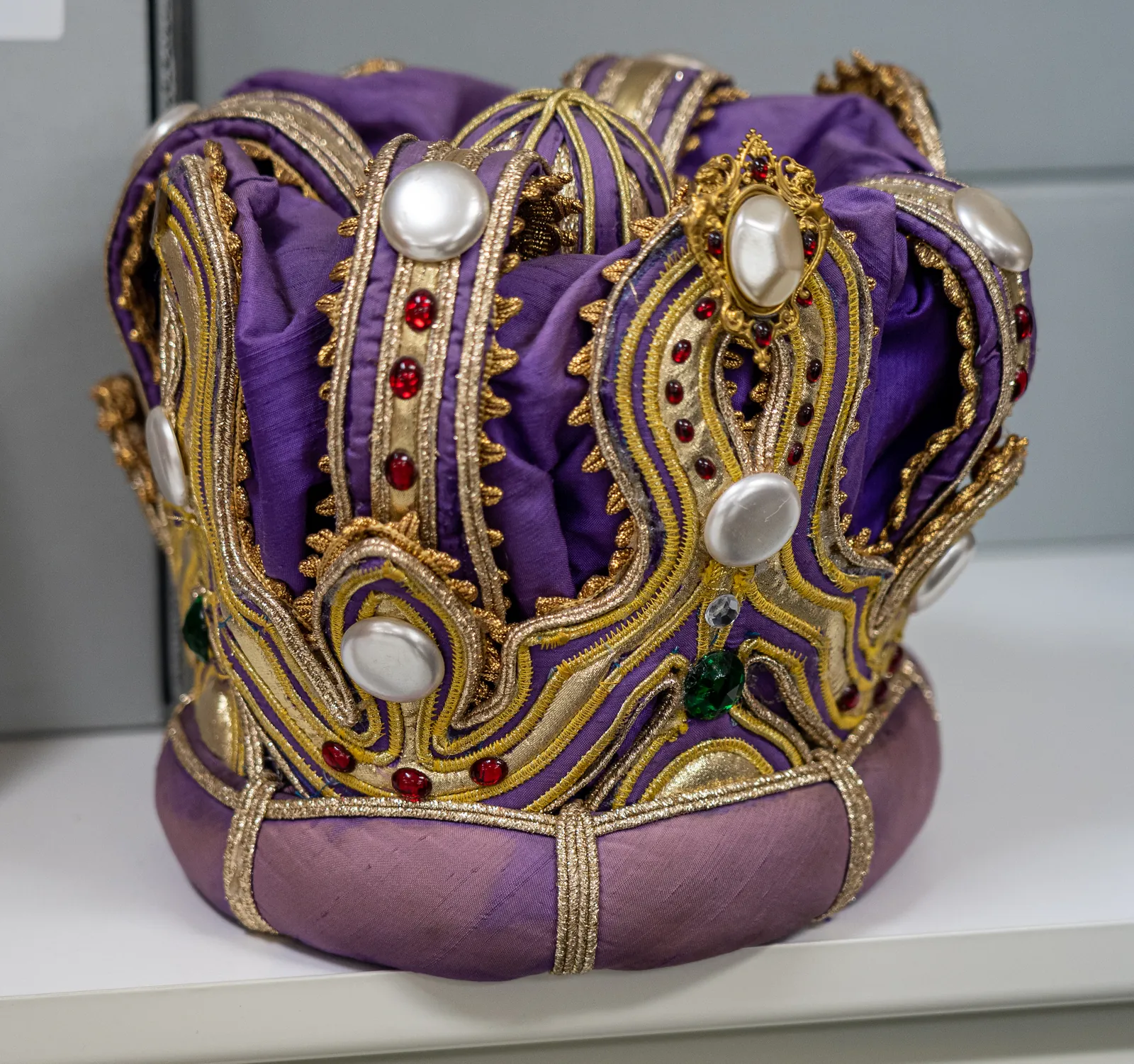 A King of Moomba’s crown on a store-room shelf: a cap of purple silk under arches of gold braid, set with pearls and red and green stones.